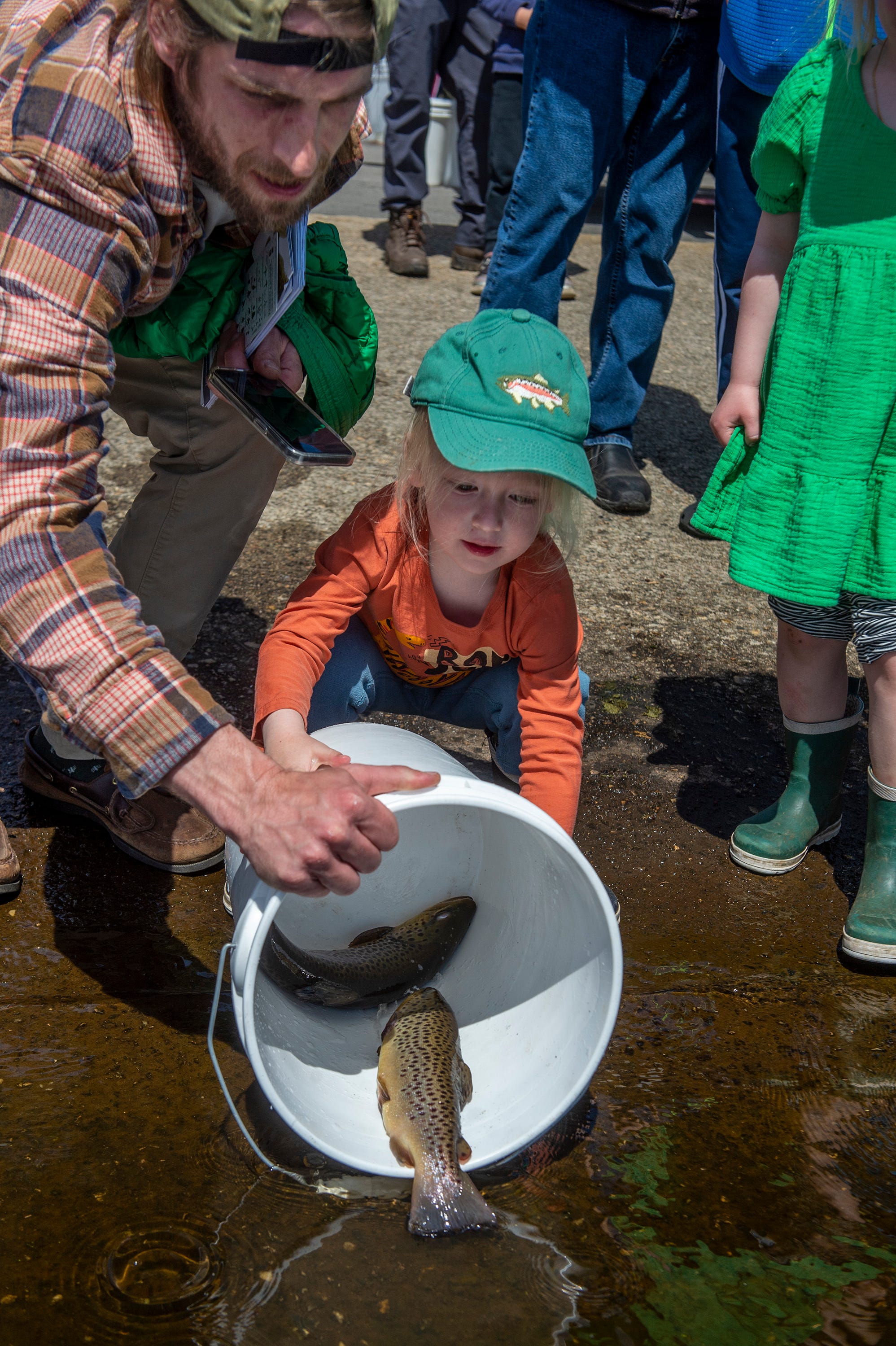 Mitchell Moore, left, and son Mitchell 3, of Southborough, release a bucket of brown trout into the Hopkinton Reservoir, April 17, 2024.