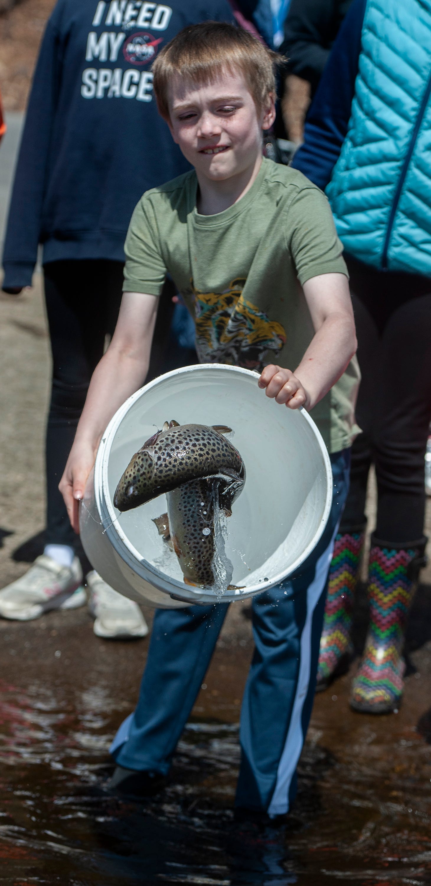 A youngster releases a bucket of brown trout from the Mass Wildlife Sunderland Hatchery into the Hopkinton Reservoir at Hopkinton State Park, April 17, 2024. Dozens of children showed up at the park to release 400 brown trout. Mass Wildlife is releasing 500,000 trout into Massachusetts waters this Spring.